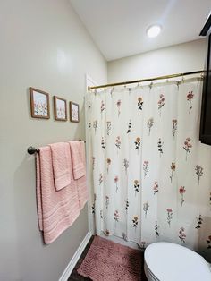 a white toilet sitting next to a pink rug in a bathroom under a shower curtain