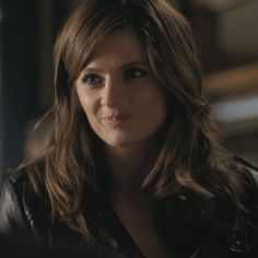 a woman with long brown hair wearing a black leather jacket and looking at the camera