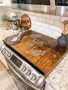 a wooden cutting board on top of an oven in a kitchen with stainless steel appliances