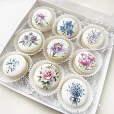 there are nine cupcakes in the box on the table with flowers painted on them