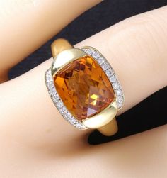 A wonderfully designed, luxurious 18k yellow gold natural bright golden citrine and diamond ring is ready to become your statement piece. The 5.50 carat citrine is stunning, measures 12x10mm antique cushion cut and set in a half bezel tension style mount. The 18 VS clarity G color diamonds, all perfectly matched, full cut round brilliant total .20 carats. Weighs 8.8 grams and is a size 7.5. Measures 17x14mm across the top, (25mm to an inch) and is marked 750. Excellent condition. Gold Cushion Cut Topaz Ring For Formal Occasions, Formal Gold Cushion Cut Topaz Ring, Gold Cushion Cut Topaz Ring, Luxury Amber Topaz Anniversary Ring, Luxury Amber Topaz Ring For Anniversary, Antique Cushion Cut, Antique Cushion, Half Bezel, Estate Rings