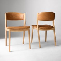 two wooden chairs sitting next to each other on a white surface with one chair facing the other