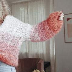 a woman with blonde hair wearing a pink and white knitted sweater in front of a window