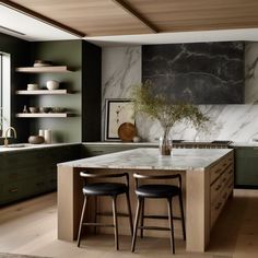 a kitchen with green cabinets and marble counter tops, two stools at the island