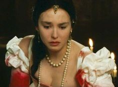 a woman wearing pearls is looking down at her cell phone in front of some candles