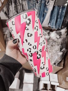 a woman holding up a pink and white cup with leopard print on it in front of clothes