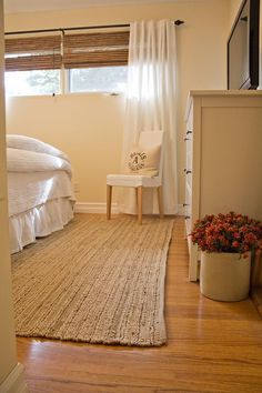 a bedroom with a bed, chair and rug on the wooden floor next to a window