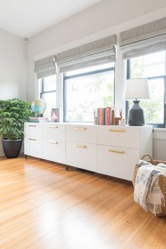 a living room filled with furniture and a lamp on top of a dresser next to a window