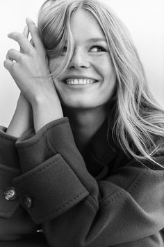 black and white photograph of a woman smiling with her hands on her face, wearing a coat