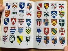 an open book with many different crests on it's pages and two hands holding one