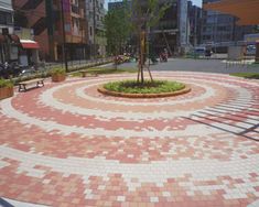 a circular bricked area in the middle of a city street with benches and trees