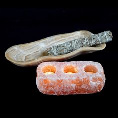 two pieces of soap sitting next to each other on a black surface with a wooden object in the background