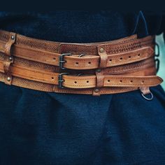 Light Brown Double Wide Medieval Girdle / Corset Type Warrior Belt An amazing display of leather craftsmanship. Featuring four hand sewn loops and Celtic knotwork embossed throughout and three half rings added to the bottom of the belt to attach additional accessories or tools. Material: Genuine Leather.Approx. Width: 4.5" (11.5cm) wide leather with two 1" (2.5cm) wide belts attached.Approx. Lengths (all are adjustable): - Small: up to 37" (100cm) - Medium: up to 47" (120cm) - Large: up to 55" (140cm) Worldwide shipping available!Not always in stock: Please allow up to 1-2 weeks before item ships. Share: Viking Pictures, Viking Belt, Medieval Belt, Brown Rings, Bead Hair Accessories, Viking Clothing, Leather Armor, Celtic Knotwork, Wide Leather Belt