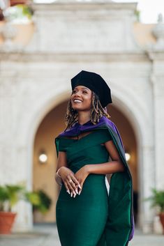 a woman in a green gown and black hat smiles at the camera while standing outside