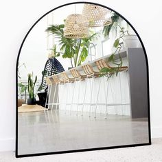 an arched mirror with plants in the background and a bench on the floor next to it