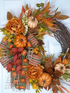 a wreath with pumpkins, flowers and leaves on it is hanging on the front door