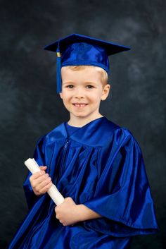 a young boy wearing a blue graduation gown and holding a diploma