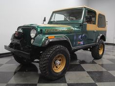 a green and yellow jeep is parked on a checkerboard floor in a garage