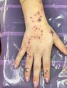 a woman's hand with stars and moon tattoos on her left palm, in front of a purple background