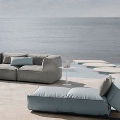 a couch sitting on top of a stone floor next to the ocean with pillows and lamps