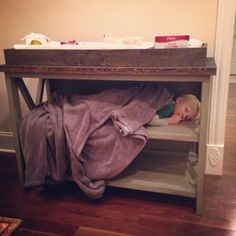 a small child is sleeping under a blanket on a table in a room with hardwood floors