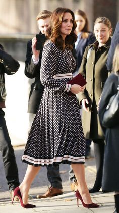 a woman in a dress and heels walking down the street with other people behind her