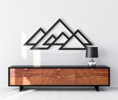 a wooden dresser sitting in front of a wall with mountains on the side and a lamp next to it