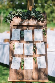 a wooden easel with seating cards attached to it and greenery on the side