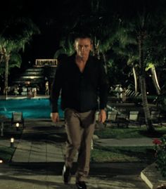 a man walking down a sidewalk next to a swimming pool in the dark at night