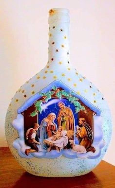 a blue glass bottle with a nativity scene on the front and sides, sitting on a wooden table