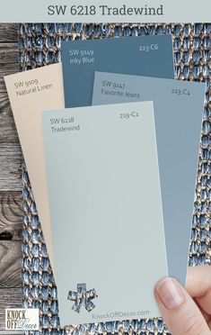 a hand holding three different shades of blue and gray paint swatches with the words sw 618 tradewind on them