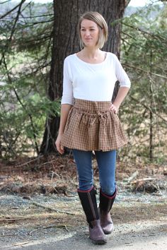 a woman standing in front of a tree with her hands on her hips and wearing boots