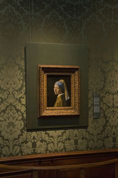 a woman with a pearl ear painting on the wall next to a bench in a museum