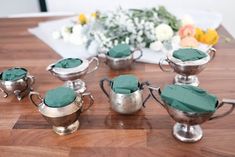 a group of silver cups sitting on top of a wooden table covered in green napkins