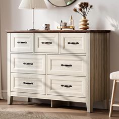 a white dresser with drawers and a mirror on the wall next to a table lamp