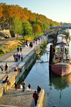 many people are walking along the water near boats