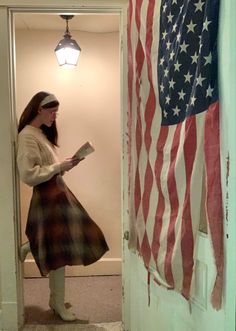 a woman is standing in front of an american flag and reading a book while looking at her phone