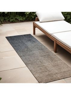 a large rug on the ground next to a bed with white pillows and plants in the background