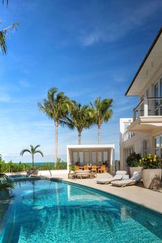 an outdoor swimming pool with chaise lounges and palm trees in front of the house