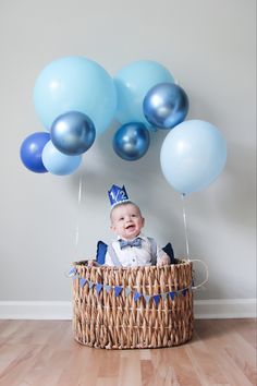 a baby is sitting in a basket with blue and white balloons on the floor,