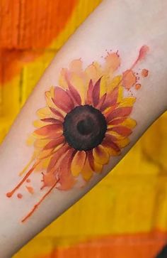 a sunflower tattoo on the arm with watercolor paint splatters all over it