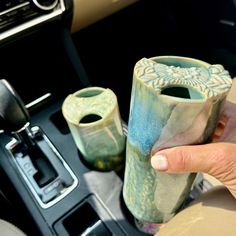 a person holding two vases in their hand next to a steering wheel control knob