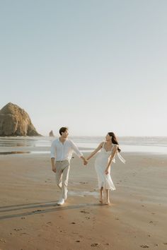 a man and woman holding hands while walking on the beach