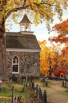 an old church surrounded by trees with autumn leaves