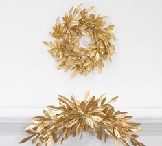 two gold wreaths hanging on the wall next to each other, one with leaves