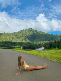 a woman laying on the side of a road next to a lush green mountain range