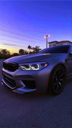 a silver car parked in front of a building at night with the sun setting behind it