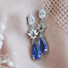 a pair of blue and white earrings on top of a piece of fabric with flowers in the background