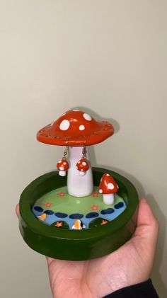 a hand holding a green tray with a red mushroom on it and white polka dots