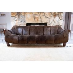 a brown leather couch sitting on top of a white rug in front of a fireplace